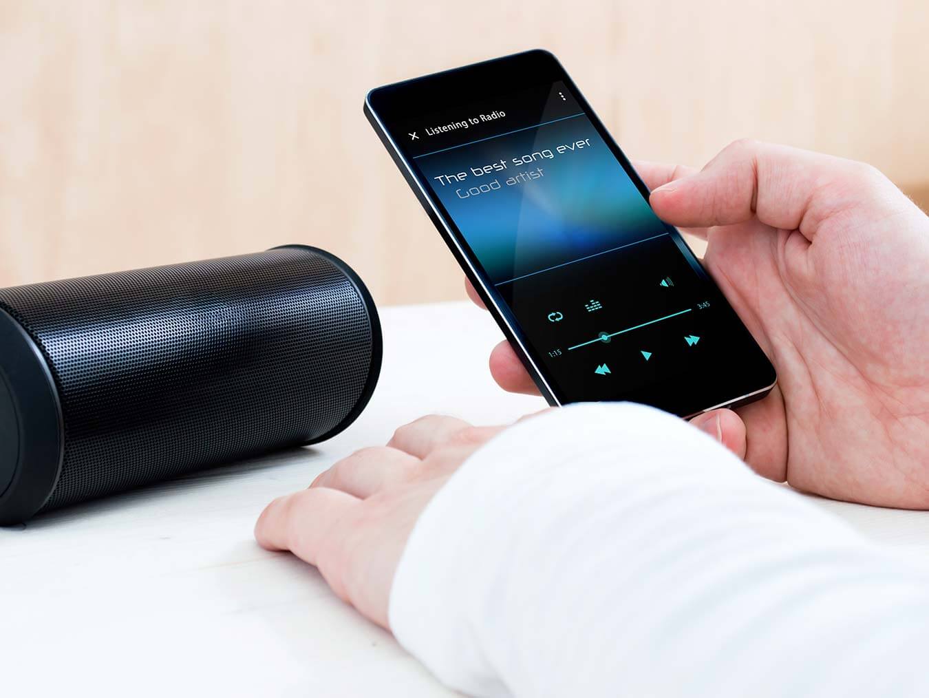 phone-music-wireless-speaker Person holds smartphone playing music next to a wireless speaker.