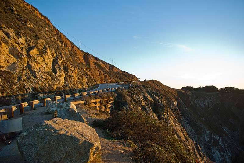 California Road Trip Highway 1 A road winds around a mountain on Highway 1 in California at sunset