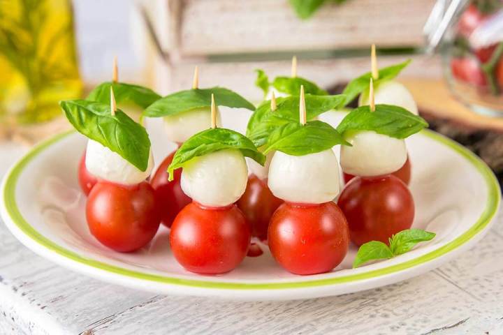 Plate of skewered mozzarella, cherry tomatoes, and basil leaves on skewers.