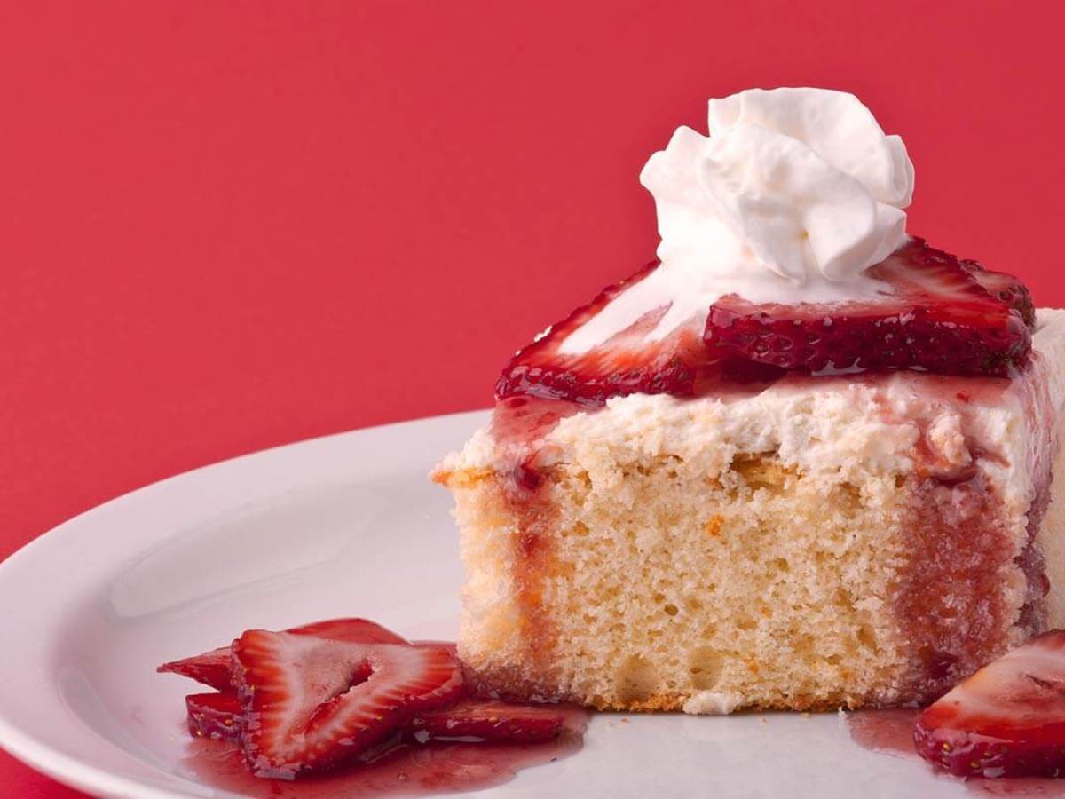 Slice of strawberry shortcake with strawberries and whipped cream on a plate against a red background.