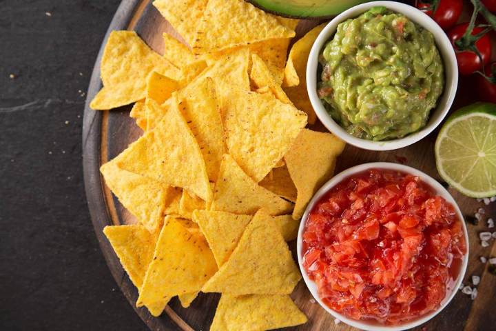 Tortilla chips with guacamole and salsa in bowls on a wooden platter.