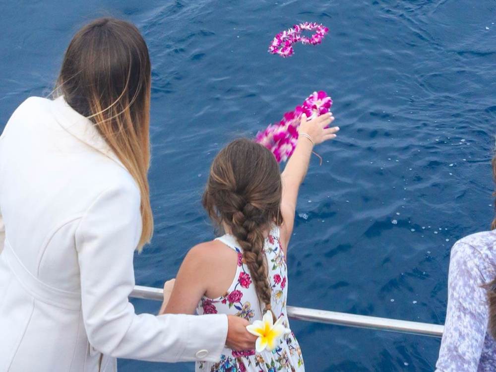 A girl throws flowers into the water from a boat during an ash scattering at sea