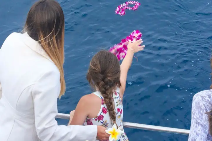 A girl throws flowers into the water from a boat during an ash scattering at sea