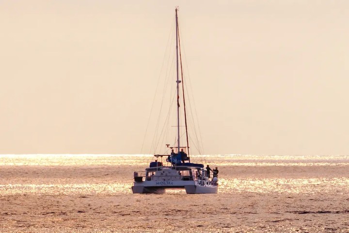 Catamaran Manute'a cruising on calm sea with golden sunlight reflecting on water.