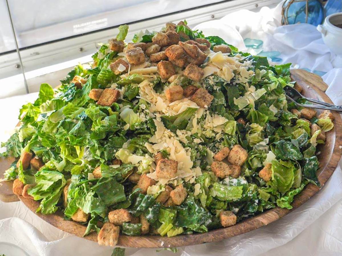 Large Caesar salad with croutons, lettuce, and cheese on a wooden platter.