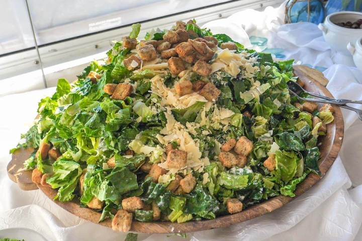 Large Caesar salad with croutons, lettuce, and cheese on a wooden platter.