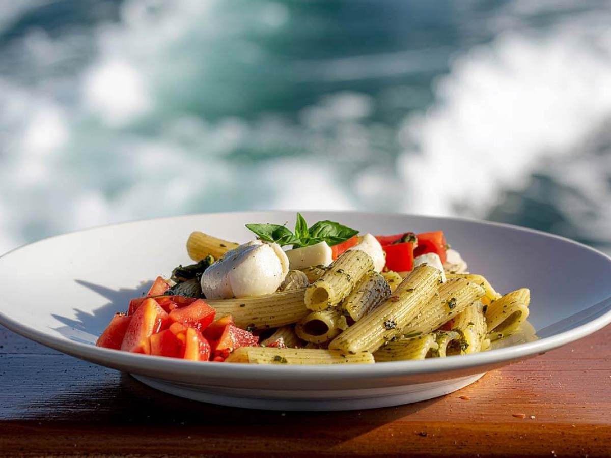 Plate of pesto pasta with tomatoes and mozzarella by the ocean.